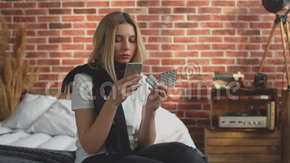 女孩坐在家里在她的智能手机上搜索互联网上的药片处方一个生病的女孩读视频的预览图