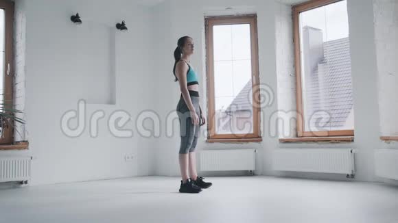 穿着运动服的漂亮女孩站在家里明亮的房间里视频的预览图