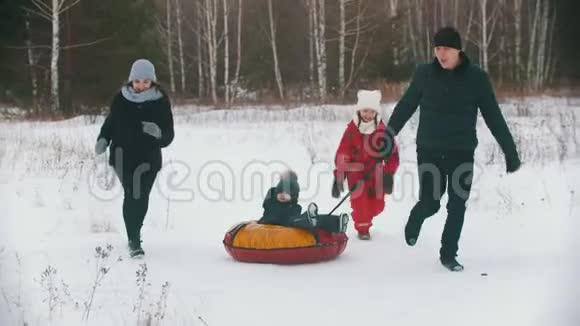 一家人在森林附近的户外跑步和玩耍男人把他的孩子卷在充气雪橇上视频的预览图