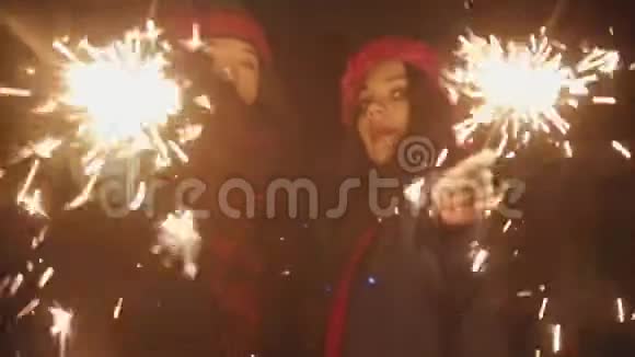 两个微笑着的年轻女性朋友在晚上玩火花和跳舞看着镜头视频的预览图