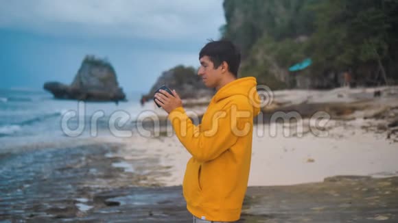 晚上穿黄色连帽衫的男摄影师在美丽的热带海滩上拍照视频的预览图