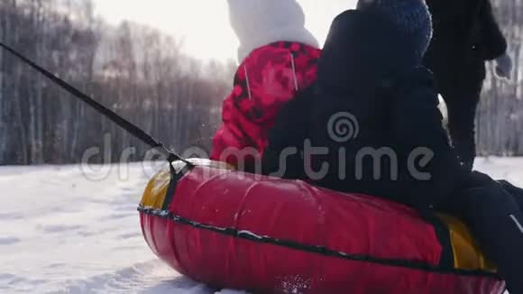 一家人在冬天的田野上玩耍父亲骑着他的孩子在充气雪橇上母亲在追视频的预览图
