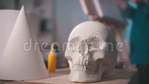 一位年轻的女艺术家在艺术工作室画一幅画一个头骨和桌子上的其他图形视频的预览图
