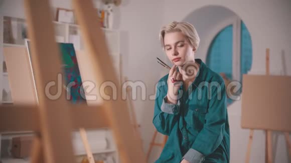 一位年轻的女艺术家一头金色的短发坐在艺术工作室里她的手沾满了油漆视频的预览图