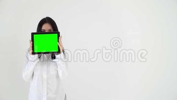 一个年轻的女孩眼睛从一个绿色屏幕的数字平板电脑后面往外看一个穿白色上衣的女孩遮住了她的脸视频的预览图
