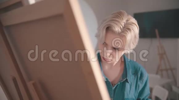一位年轻的金发女艺术家在艺术工作室画一幅画视频的预览图
