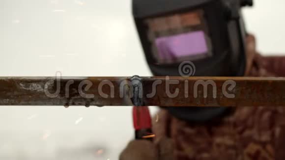 焊接机上的金属接缝在背景中一个戴着焊接面罩和冬季工作夹克的人接触到了视频的预览图