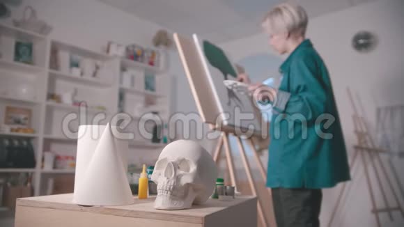 一位年轻的女艺术家在艺术工作室一个头骨和桌子上的其他人物视频的预览图