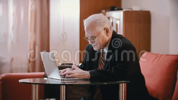 年迈的祖父戴着眼镜和夹克的老祖父正在电脑上打字视频的预览图