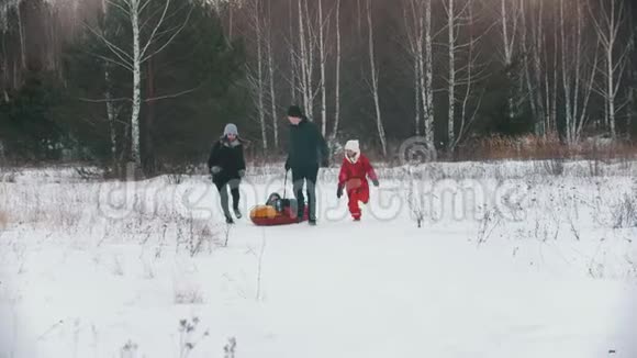 一家人在森林附近的户外玩耍男人把他的孩子卷在充气雪橇上视频的预览图