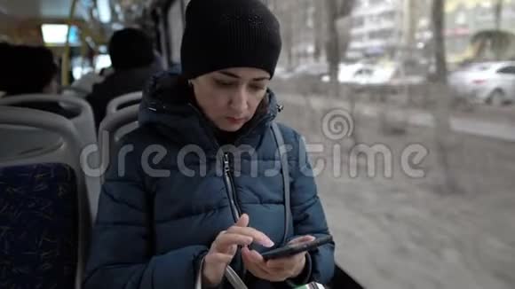 特写镜头一个手里拿着手机的成年女孩正坐在一辆公交车的窗口温暖地穿过城市视频的预览图