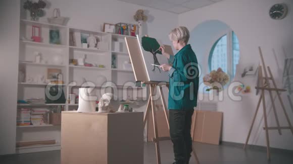 一位年轻的女艺术家在艺术工作室做一幅树画一个头骨和桌子上的其他图形视频的预览图