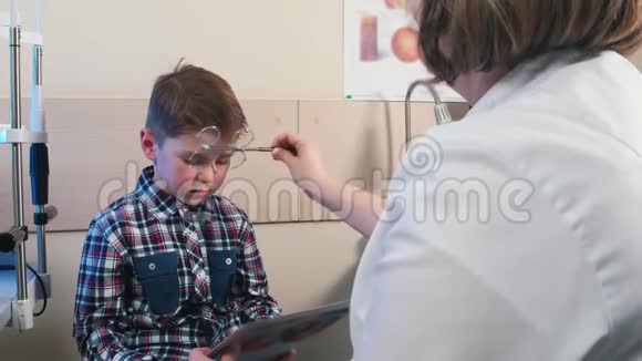 眼科医生治疗检查一个小男孩的眼睛一个男孩通过不同的平板电脑读信视频的预览图