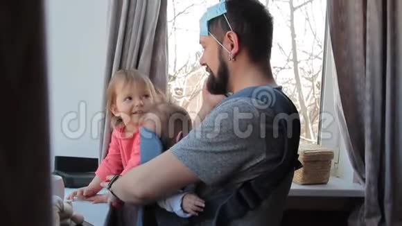 爸爸戴着面具带着婴儿和蹒跚学步的女孩在家玩冠状病毒流行2019nCOVCovid19大流行视频的预览图