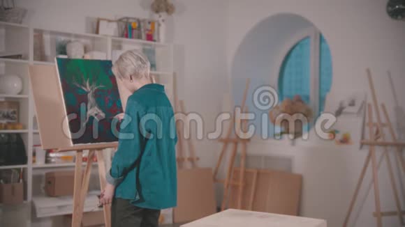 一位年轻的女艺术家在画中添加了最后的修饰坐在椅子上视频的预览图