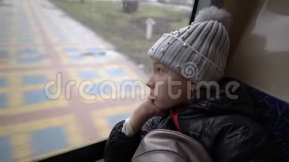 一个悲伤的小女孩在冬天的城市景观上从公共汽车的窗户外看上去很体贴她坐在后面视频的预览图