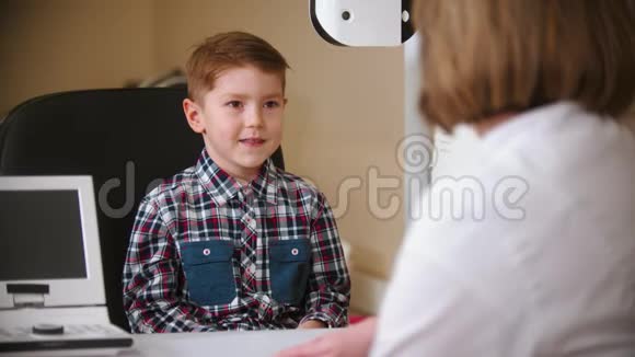 眼科诊所的一种治疗方法成熟的女医生和一个小男孩坐在桌子旁视频的预览图