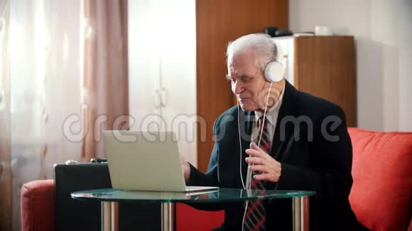 年迈的祖父戴着耳机微笑着看着笔记本电脑屏幕的老祖父视频的预览图