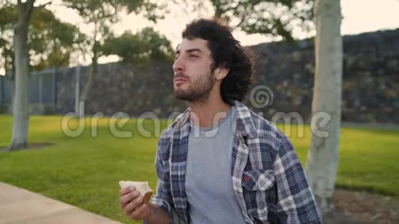 在公园炎热的夏日一位快乐英俊的年轻人在一边吃三明治视频的预览图