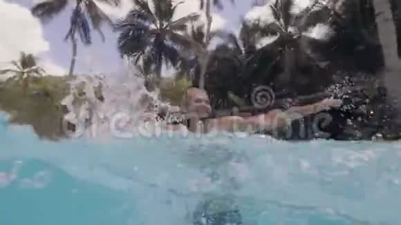 在度假酒店的室外游泳池里开朗的男人泼水水景快乐的人在游泳中玩视频的预览图