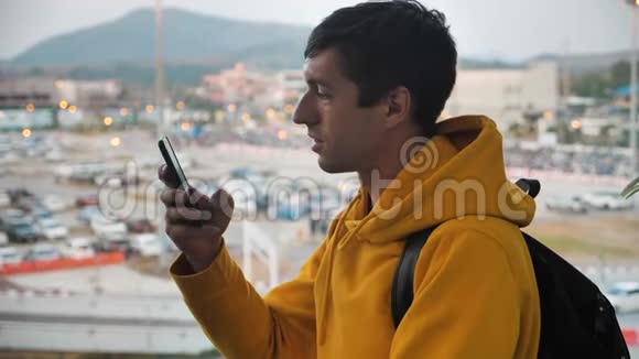 男子游客带背包的肖像站在一个大窗户前的室内使用智能手机旅行概念视频的预览图