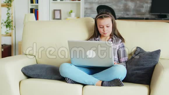 戴着牙套的可爱小女孩用笔记本电脑坐在沙发上视频的预览图