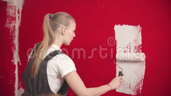女人正在用白色滚筒画一堵红墙视频的预览图