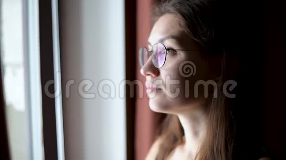 一个戴眼镜的年轻女子望着窗外期待着来自一个黑暗的房间视频的预览图