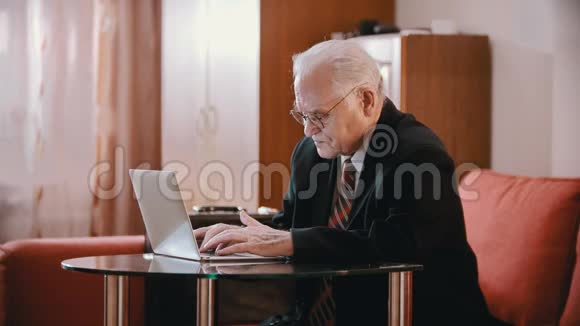 年迈的祖父穿着夹克和领带的祖父正慢慢地在电脑上打字视频的预览图