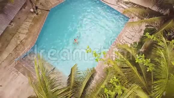 在热带酒店的蓝水漂浮游泳池里游泳的无人视野男子空中景观夏季平房和游泳视频的预览图