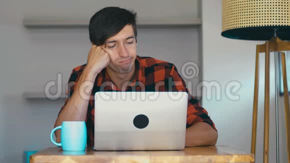 年轻无聊的商人坐在家里的桌子旁视频的预览图