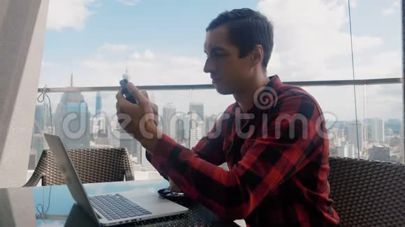 忙碌的商人使用智能手机在笔记本电脑上工作在摩天大楼高层的咖啡馆喝咖啡视频的预览图