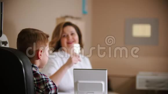 眼科医生治疗成熟的女医生和一个小男孩坐在桌子旁给男孩一个眼罩视频的预览图