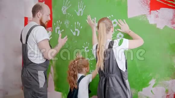 一家人把他们的白色手印放在绿色的墙上并模仿视频的预览图