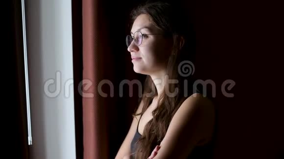 戴眼镜的年轻女子从一间漆黑的房间望着窗外轻轻地笑着视频的预览图