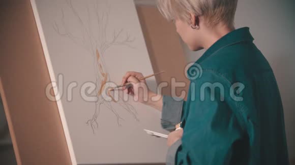 一位年轻的女艺术家在艺术工作室里用米色画树干视频的预览图