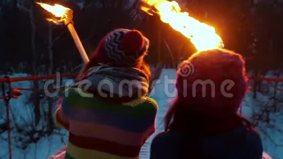 傍晚两个年轻的妇女手持燃烧的火把穿过大桥走向冬林视频的预览图
