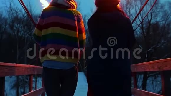 晚上两个年轻的女人拿着火把穿过大桥走到冬天的森林视频的预览图