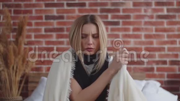 一个带着围巾围在脖子上的围巾裹着毯子揉着肩膀温暖自己一个年轻的女人视频的预览图