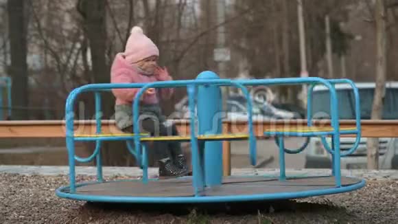 孤独的小女孩在孩子们的操场上旋转旋转木马视频的预览图