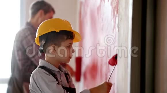 一个小男孩和他微笑的父亲在新公寓里画红色的墙一个戴着头盔的男孩视频的预览图