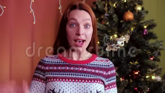 一位红头发的年轻女子看着相机为圣诞节挥手致意背景中的圣诞树视频的预览图
