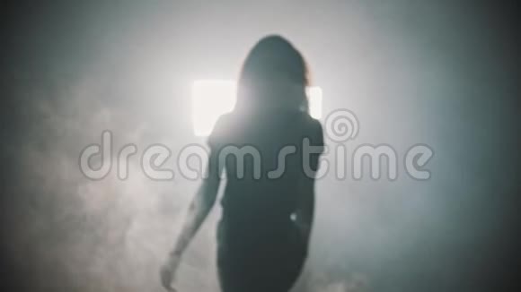 一个年轻迷人的女人长发从烟雾中走出来开始在明亮的灯光背景下跳舞视频的预览图