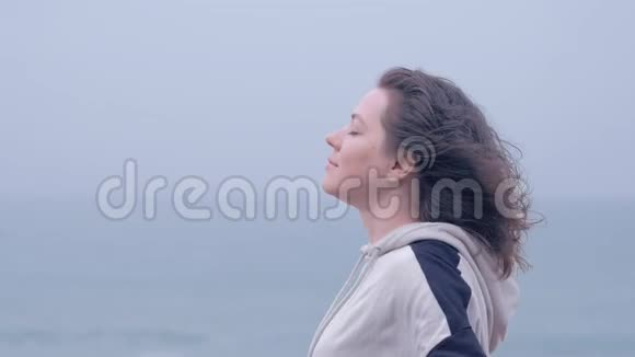 一个蓝眼睛女人在海滩上享受灰色雨天的肖像视频的预览图