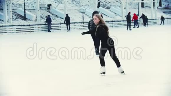 一位年轻的金发女子职业花样滑冰运动员在户外溜冰场上滑冰围着人们转视频的预览图