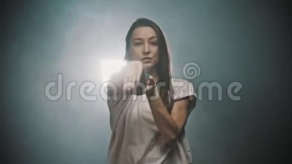 一个穿着白色t恤的灵活女人双手在烟雾弥漫的工作室里跳舞视频的预览图