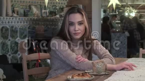 可爱的年轻亚洲漂亮女孩坐在桌旁带着面包喝咖啡微笑着视频的预览图