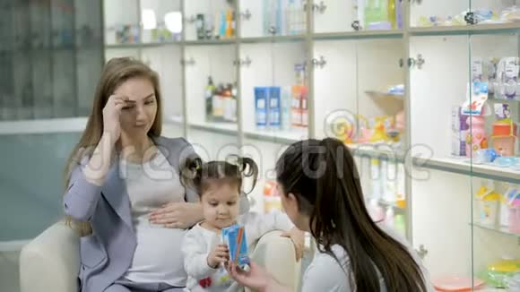 年轻的女药剂师给怀孕的顾客提供建议带着可爱的女婴医药商店概念视频的预览图