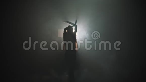 一个年轻女子的剪影她的手在明亮的灯光背景下跳舞走出黑暗视频的预览图