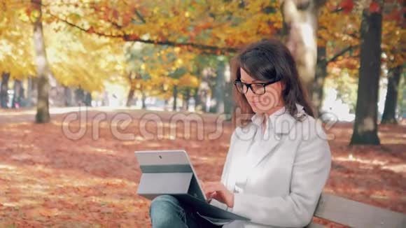 戴眼镜的女人在秋天公园用笔记本工作视频的预览图